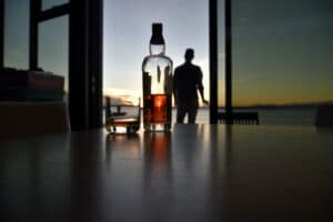 Alcohol bottle with glass with man in background on outdoor deck.